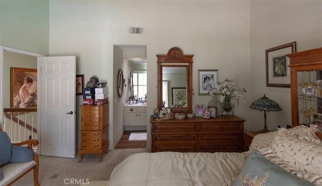 carpeted bedroom featuring visible vents, a towering ceiling, and ensuite bath