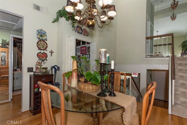 dining space featuring a chandelier, a high ceiling, wood finished floors, visible vents, and stairway