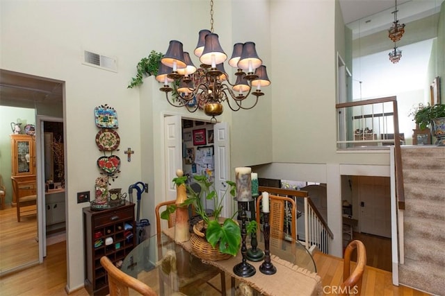 dining area featuring visible vents, a high ceiling, an inviting chandelier, wood finished floors, and stairs