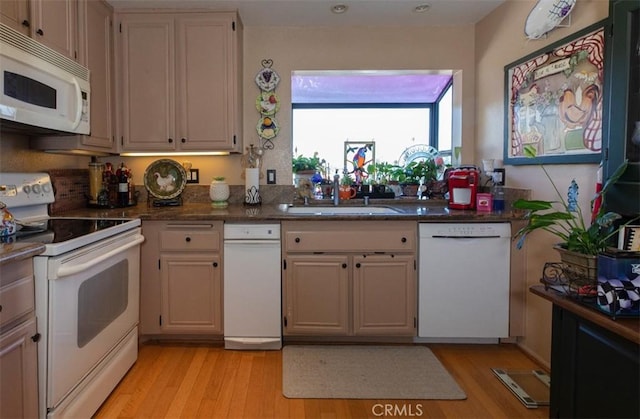 kitchen with white appliances, dark countertops, a sink, and light wood-style flooring