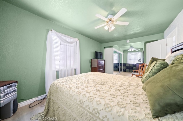 bedroom with a textured wall, wood finished floors, a ceiling fan, and baseboards