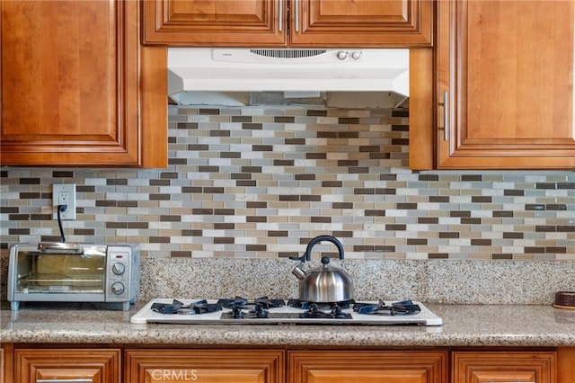 kitchen featuring under cabinet range hood, a toaster, tasteful backsplash, and brown cabinetry