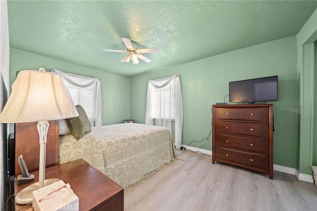 bedroom featuring ceiling fan, a textured ceiling, baseboards, and wood finished floors