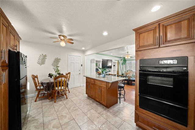 kitchen with freestanding refrigerator, brown cabinets, a warming drawer, and a breakfast bar area