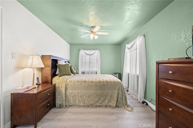 bedroom with light wood finished floors, a ceiling fan, a textured ceiling, and a textured wall