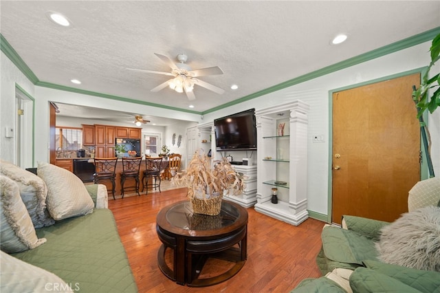 living area featuring a textured ceiling, ceiling fan, ornamental molding, and wood finished floors