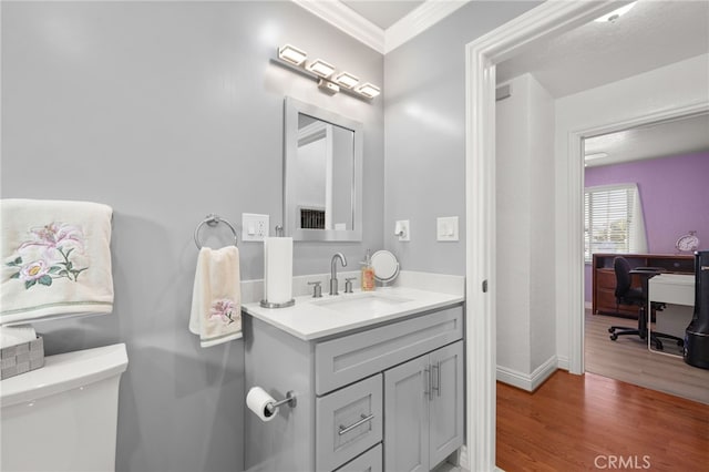 half bathroom featuring crown molding, toilet, vanity, wood finished floors, and baseboards