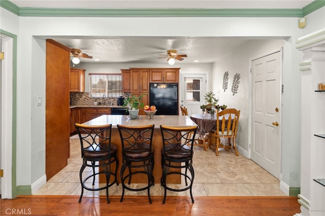 kitchen with brown cabinetry, a center island, freestanding refrigerator, a kitchen bar, and backsplash