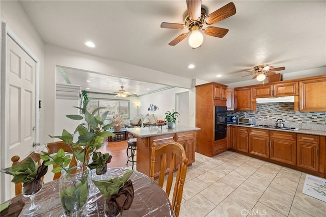 kitchen featuring recessed lighting, light countertops, backsplash, brown cabinetry, and under cabinet range hood