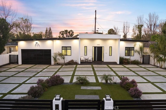 back of house at dusk with a fenced front yard, a yard, a garage, and stucco siding