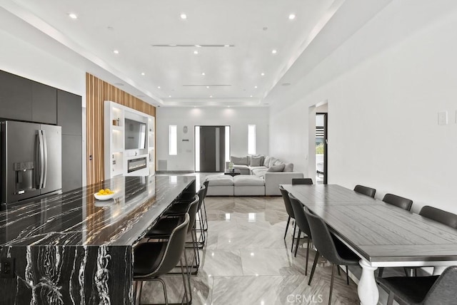 kitchen featuring stainless steel fridge with ice dispenser, modern cabinets, a breakfast bar area, marble finish floor, and dark cabinetry