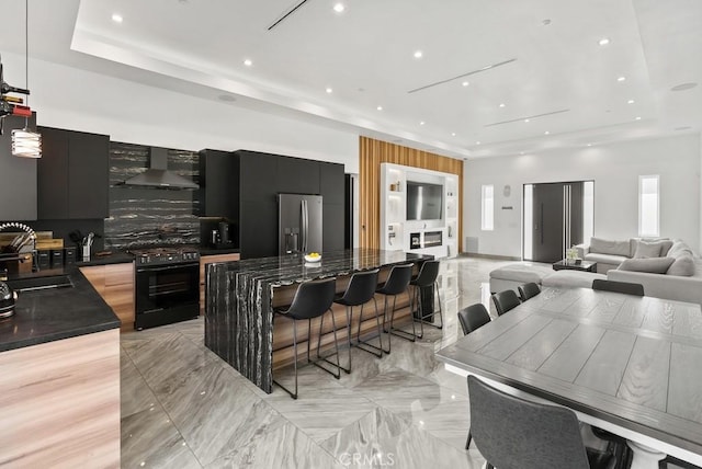 kitchen with black gas range, dark countertops, wall chimney exhaust hood, and modern cabinets