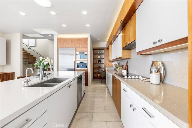 kitchen with light countertops, appliances with stainless steel finishes, white cabinets, a sink, and under cabinet range hood