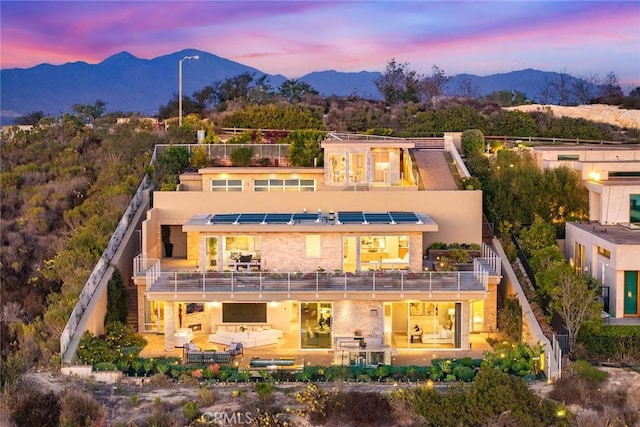 back of house at dusk featuring a patio area, a mountain view, a balcony, and a fenced backyard