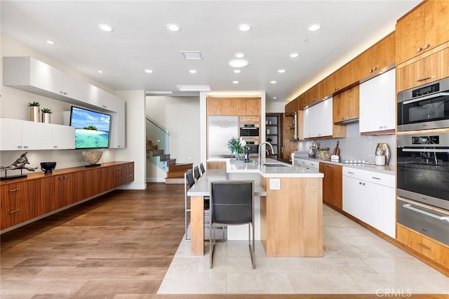 kitchen featuring a warming drawer, light countertops, brown cabinetry, an island with sink, and a kitchen bar