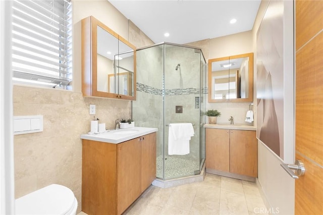 full bathroom featuring a sink, two vanities, a shower stall, and tile walls