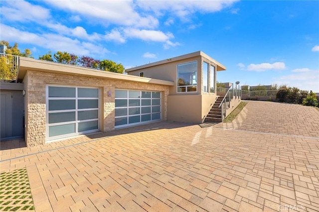 exterior space featuring a garage, stairway, decorative driveway, and stucco siding