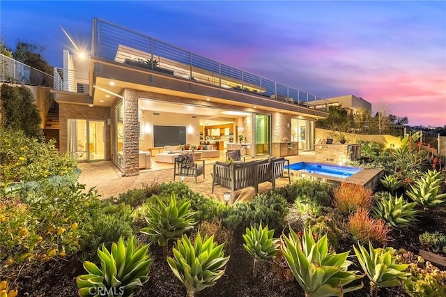 back of house at dusk with a patio, outdoor lounge area, an outdoor hot tub, fence, and a balcony