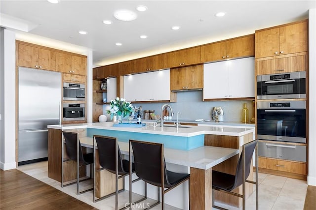 kitchen featuring a sink, light countertops, appliances with stainless steel finishes, a warming drawer, and an island with sink