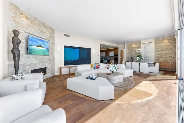 living room with a stone fireplace, wood finished floors, and visible vents