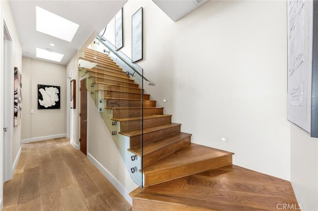 stairs with a skylight, baseboards, and wood finished floors