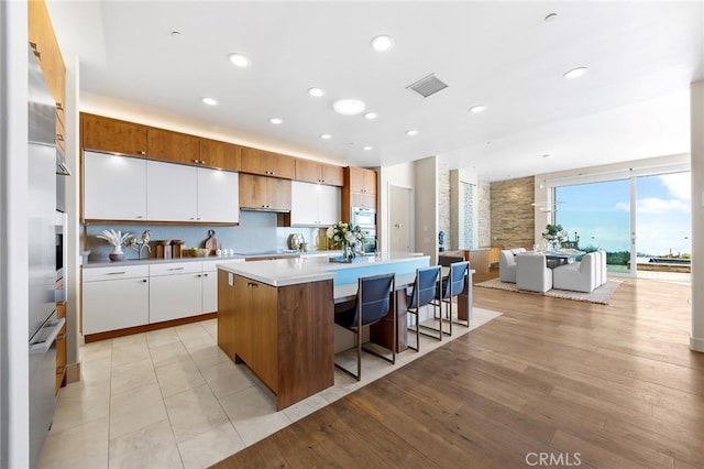 kitchen with light countertops, white cabinets, an island with sink, and recessed lighting