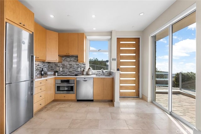 kitchen featuring appliances with stainless steel finishes, a sink, light countertops, light brown cabinets, and backsplash