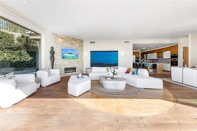 living area with light wood finished floors, a stone fireplace, visible vents, and recessed lighting