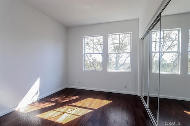 unfurnished room featuring dark wood-style floors, plenty of natural light, and baseboards