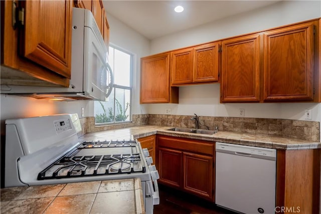 kitchen with white appliances, brown cabinetry, a sink, and recessed lighting