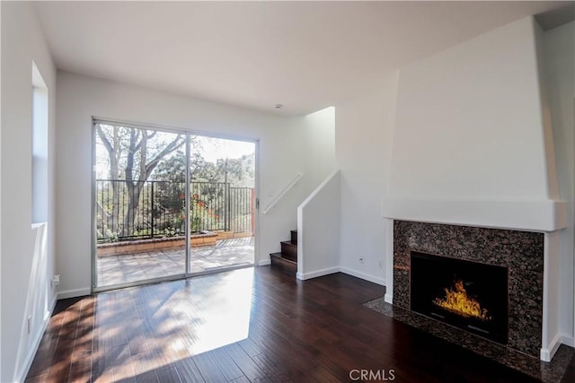 unfurnished living room with stairs, a fireplace, wood finished floors, and baseboards