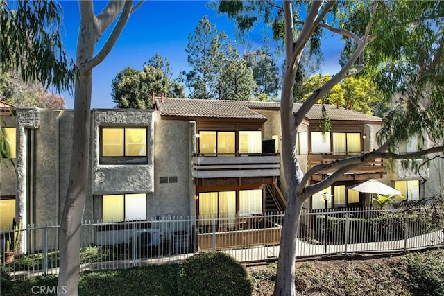 rear view of house featuring a fenced front yard, a tiled roof, and stucco siding