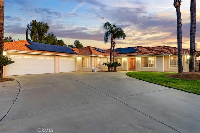 view of front of property featuring driveway, a garage, solar panels, a tiled roof, and stucco siding