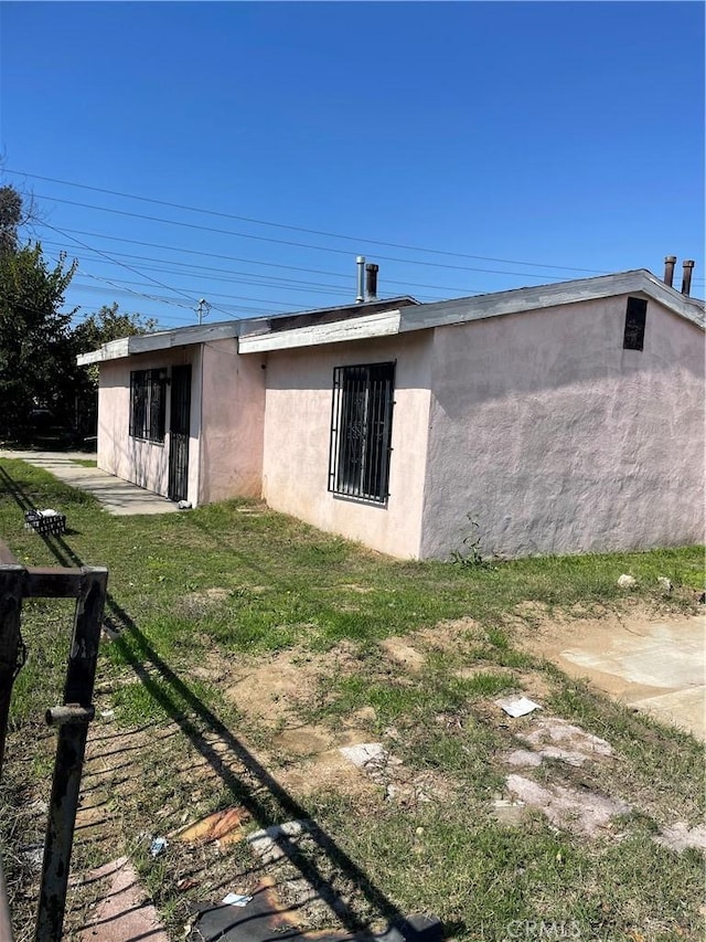 rear view of property featuring a lawn and stucco siding