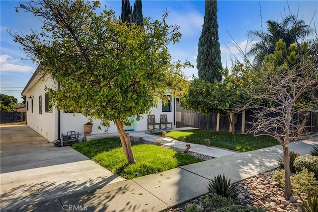 obstructed view of property featuring fence, a front lawn, and stucco siding