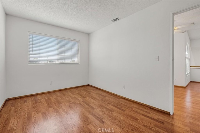 empty room featuring a textured ceiling, light wood finished floors, visible vents, and baseboards