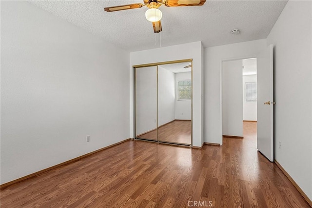 unfurnished bedroom with a textured ceiling, a closet, wood finished floors, and a ceiling fan