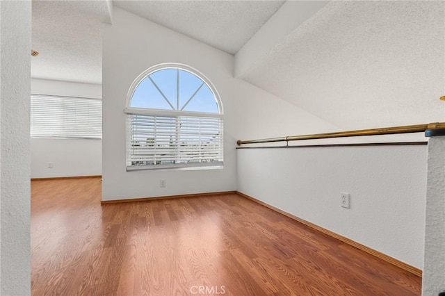 unfurnished room featuring light wood-style floors, vaulted ceiling, a textured ceiling, and baseboards