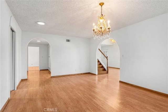 empty room with light wood-style floors, arched walkways, and visible vents