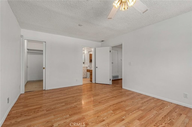 unfurnished bedroom featuring a spacious closet, light wood finished floors, visible vents, and a ceiling fan