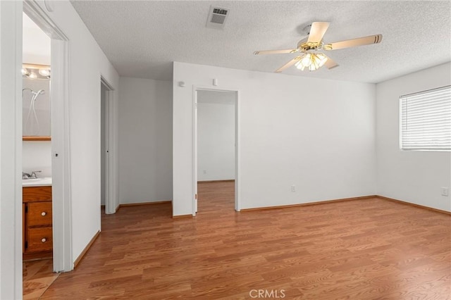 unfurnished bedroom with light wood finished floors, baseboards, visible vents, a textured ceiling, and a sink