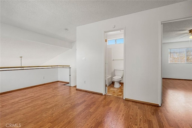 interior space featuring ceiling fan, a textured ceiling, baseboards, and wood finished floors