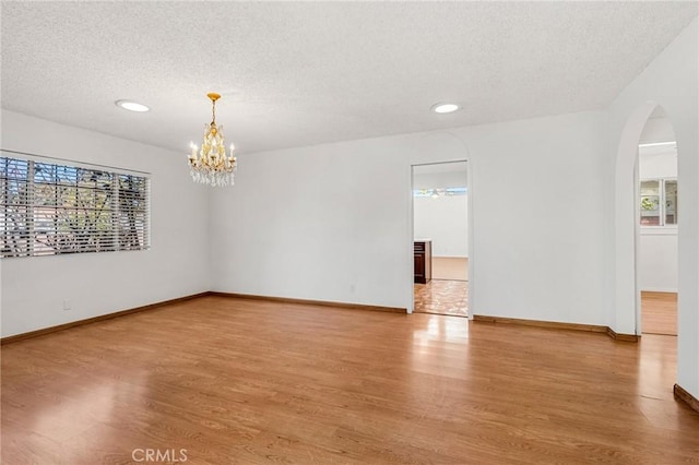 unfurnished room featuring a textured ceiling, arched walkways, wood finished floors, baseboards, and an inviting chandelier