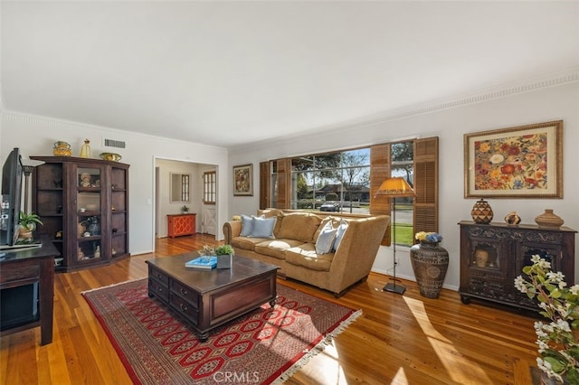 living room with wood finished floors, visible vents, and crown molding