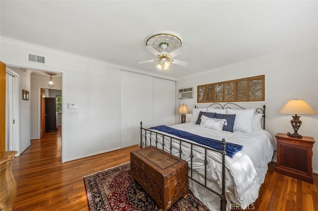 bedroom featuring dark wood-style flooring, a closet, visible vents, a wall mounted AC, and ornamental molding