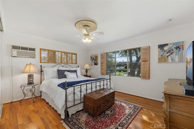 bedroom featuring a wall unit AC, a ceiling fan, baseboards, ornamental molding, and light wood-type flooring