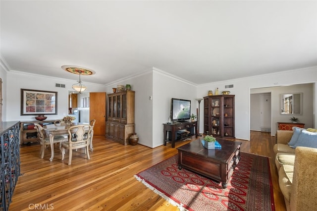 living room featuring light wood-style floors, visible vents, and ornamental molding