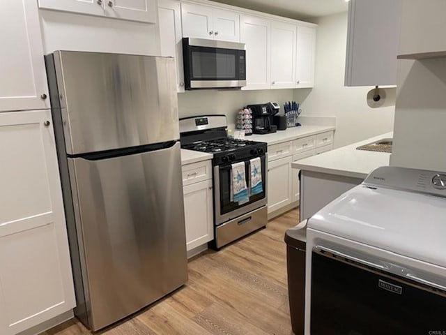 kitchen with stainless steel appliances, light countertops, light wood-style floors, white cabinets, and washer / dryer