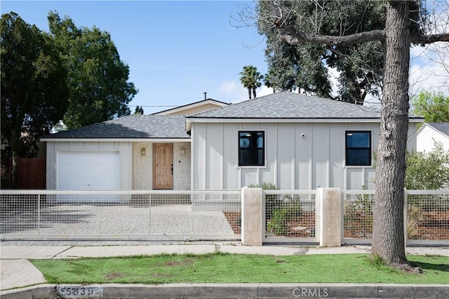 view of front of property with an attached garage, board and batten siding, a fenced front yard, and roof with shingles