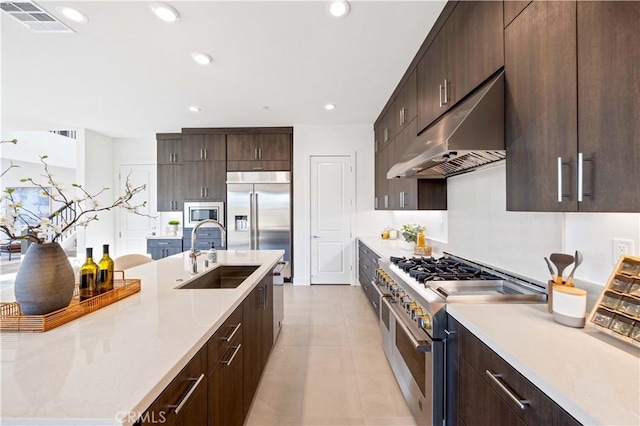 kitchen featuring built in appliances, under cabinet range hood, a sink, visible vents, and light countertops